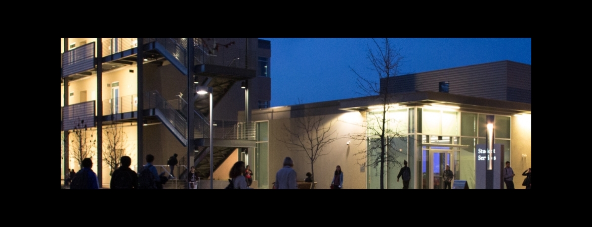 The Student Services Building at night with people crossing the street.  The Math Center is located inside the SSB.